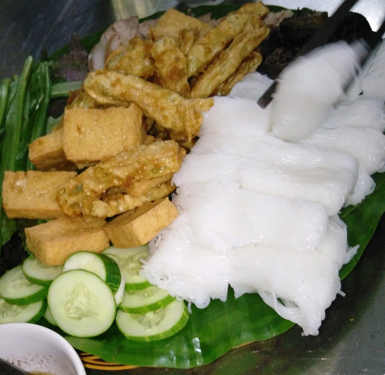 Bún lá cắt miếng xếp cạnh đậu rán và dưa leo trên lá chuối