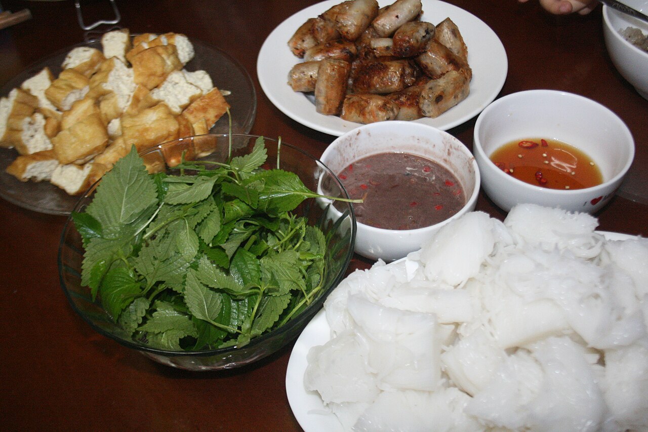 Bún lá, rau kinh giới, đậu rán, nem và chén mắm tôm trên bàn ăn
